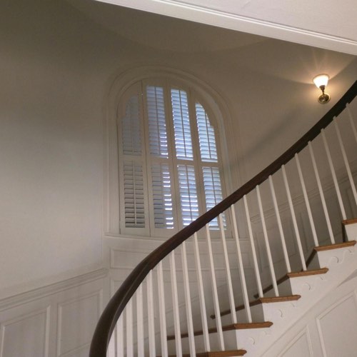White plantation shutters decorating rounded window located in curved stairwell.